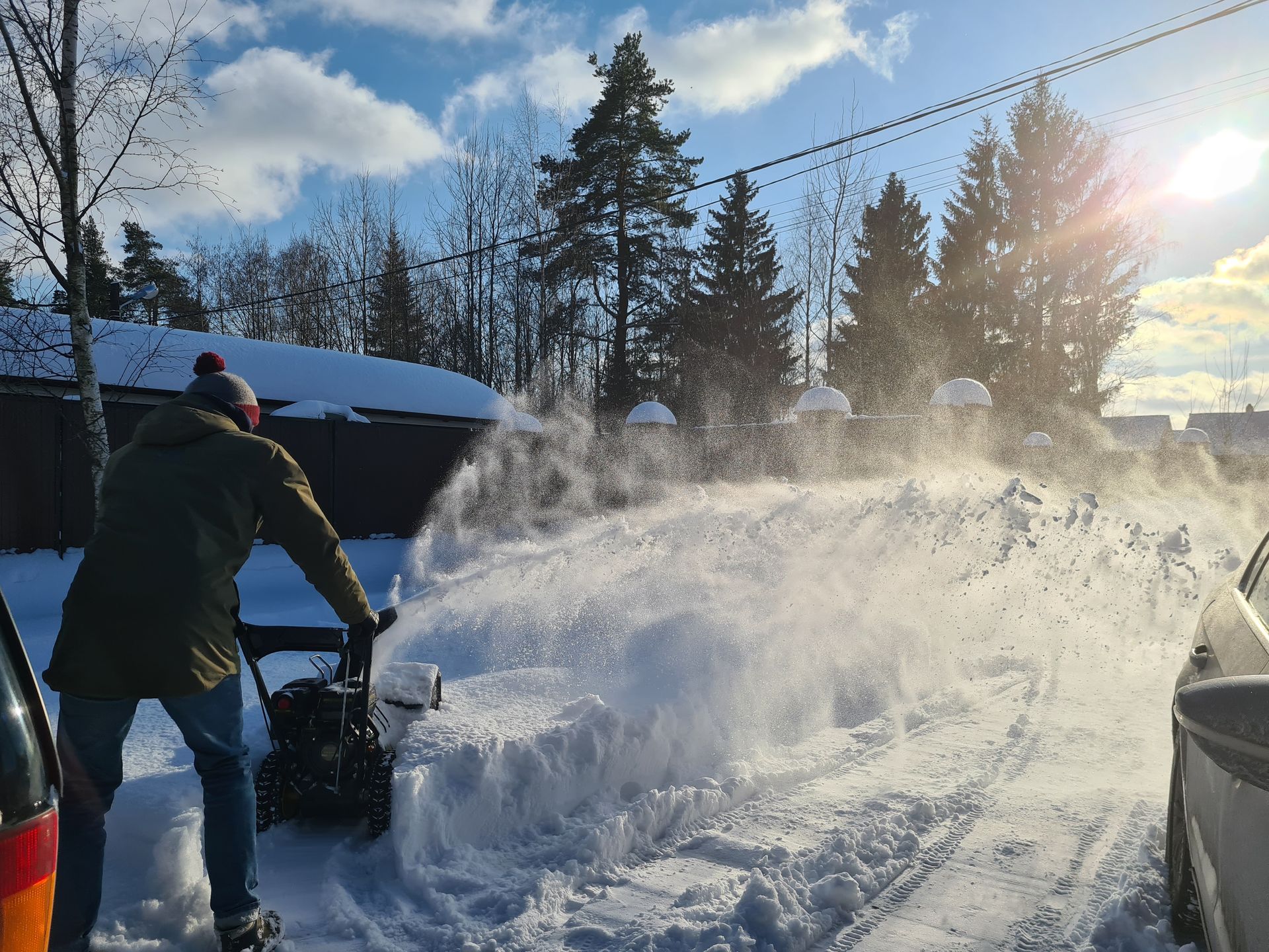 Person using a snowblower, spraying snow on a sunny winter day.