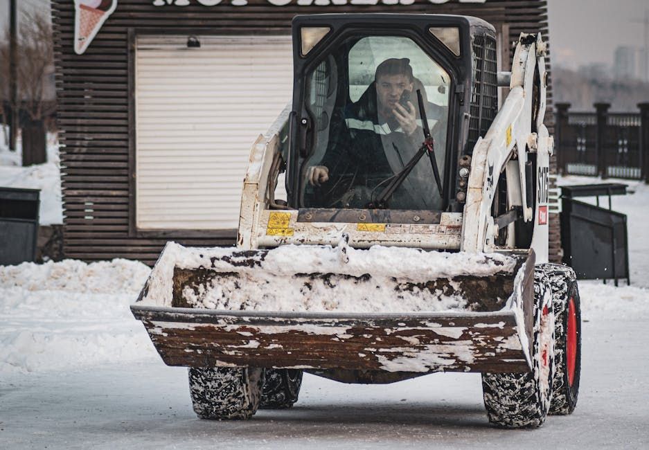 Bobcat skid-steer loader removing snow; driver in cab, outdoor winter setting.