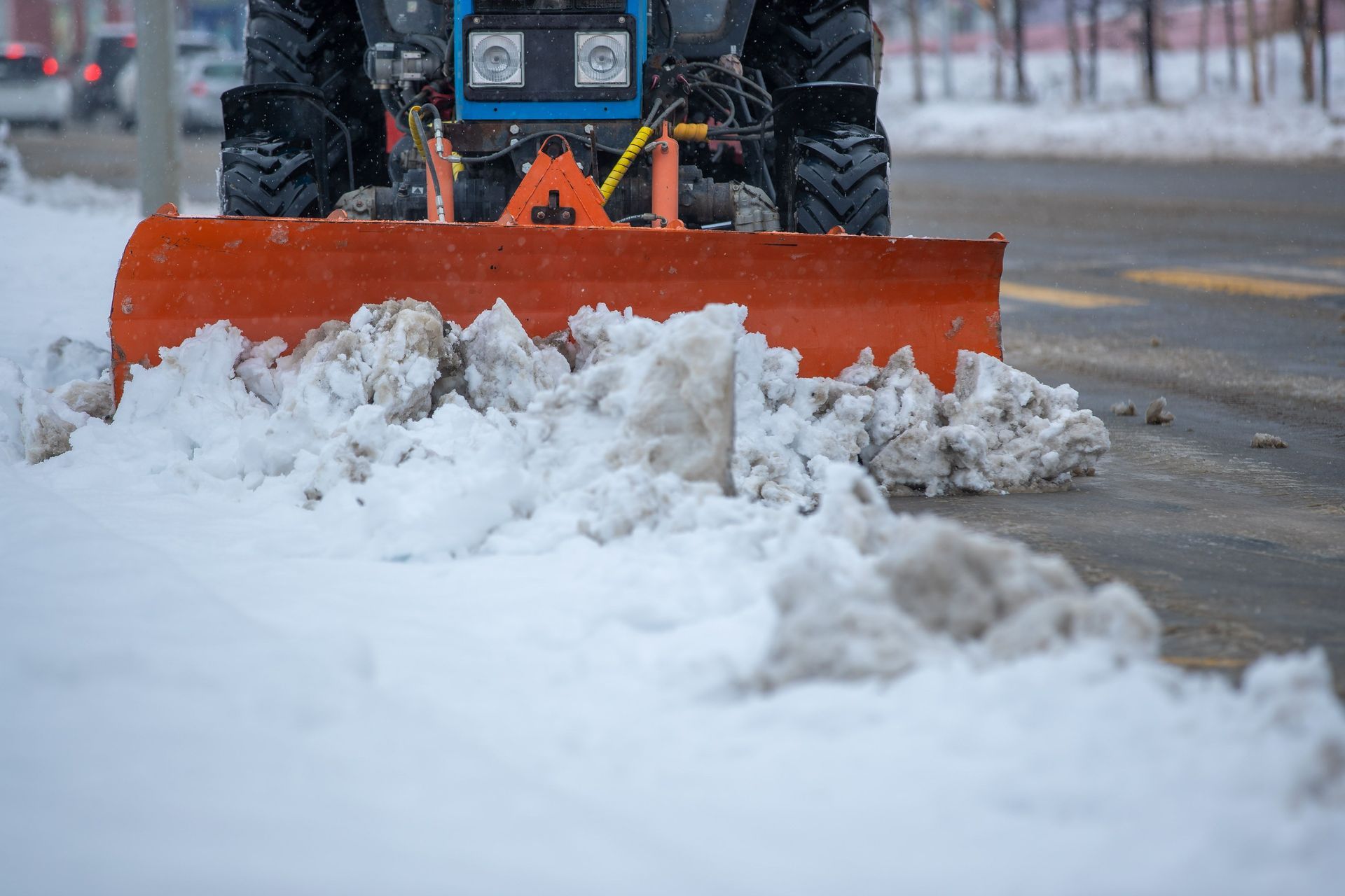 Orange snowplow clearing snow on a road, with snow piled in front of it