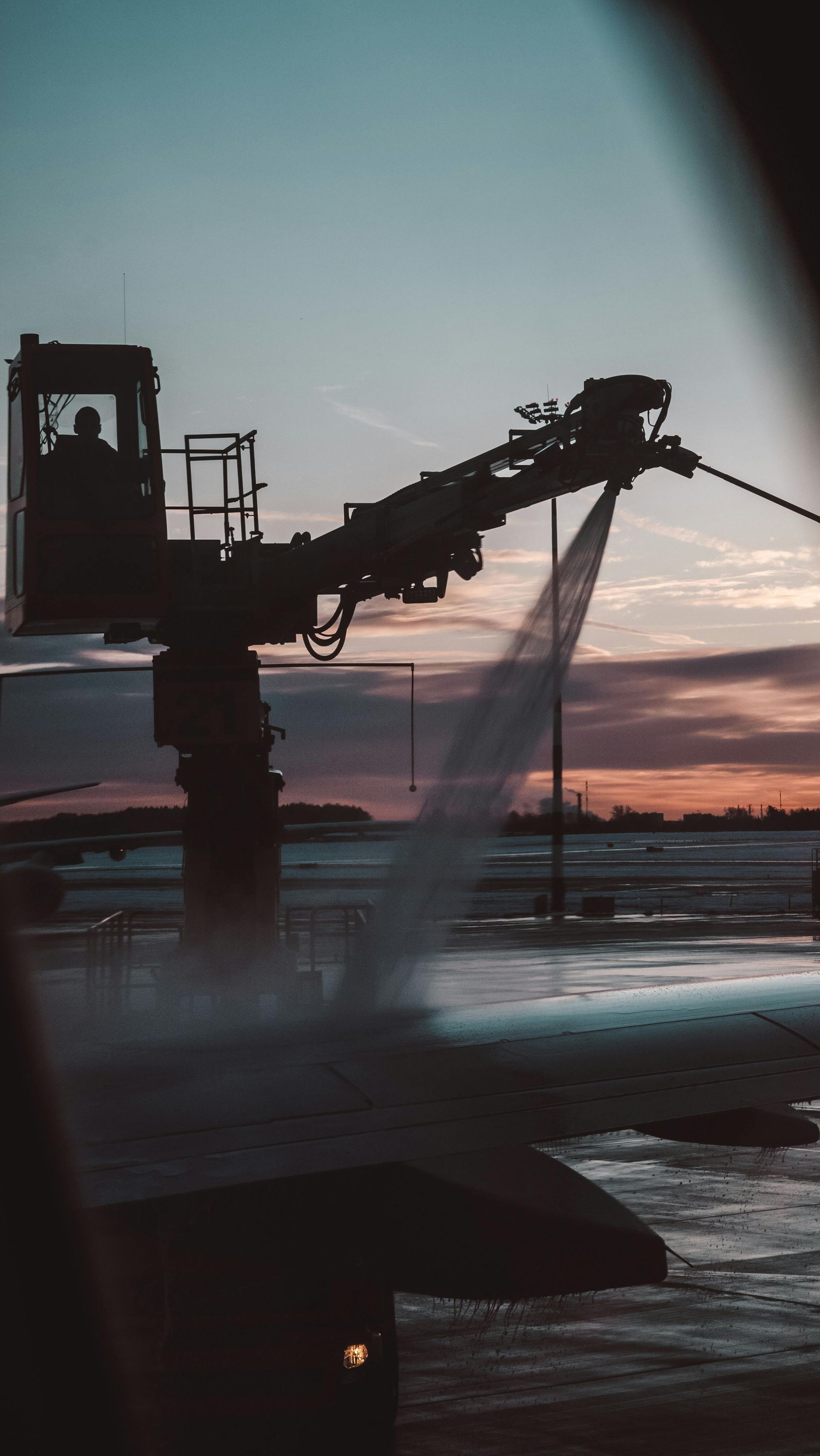 Silhouette of a snow removal machine spraying water on a frozen surface at dusk.