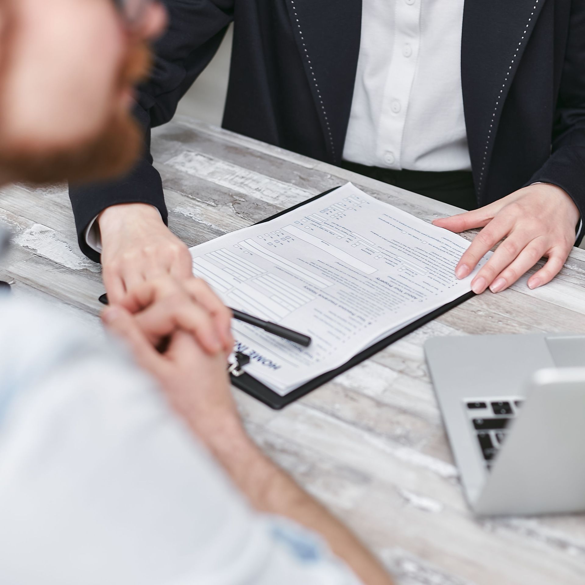 Two people in a meeting reviewing a document beside a laptop on a table