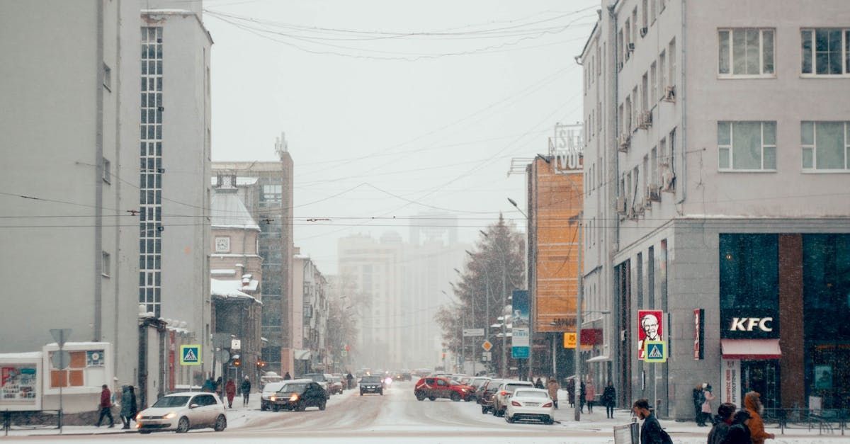 Snowy city street with cars, pedestrians, and buildings. KFC sign visible.