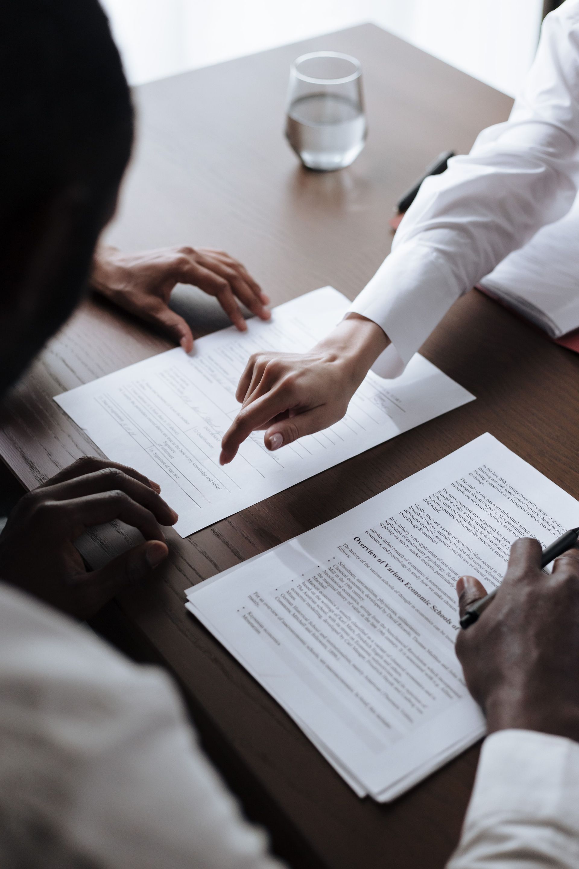 Hands reviewing documents on a conference table with a glass of water nearby