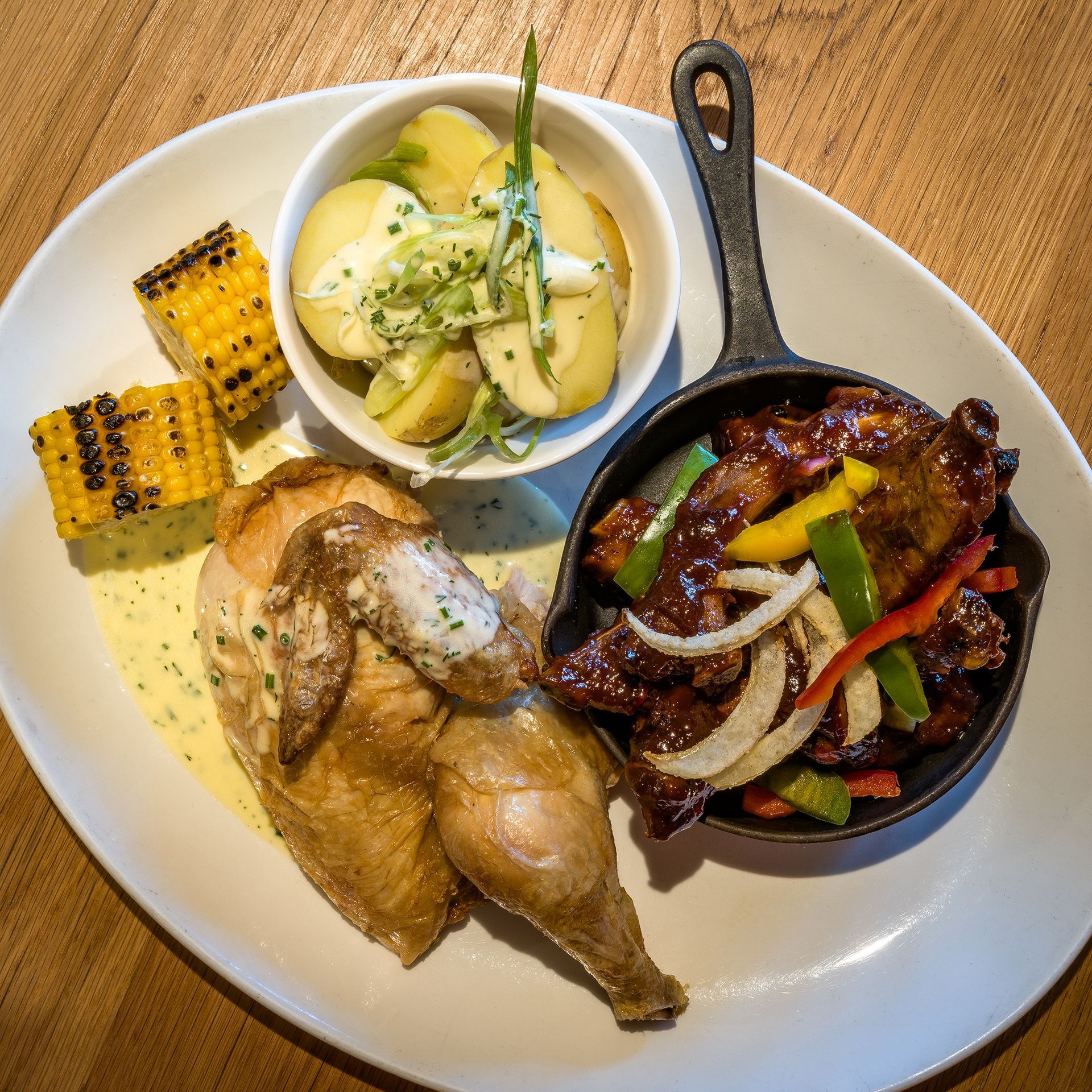 a plate of ribs and chicken with corn on the cob and potatoes