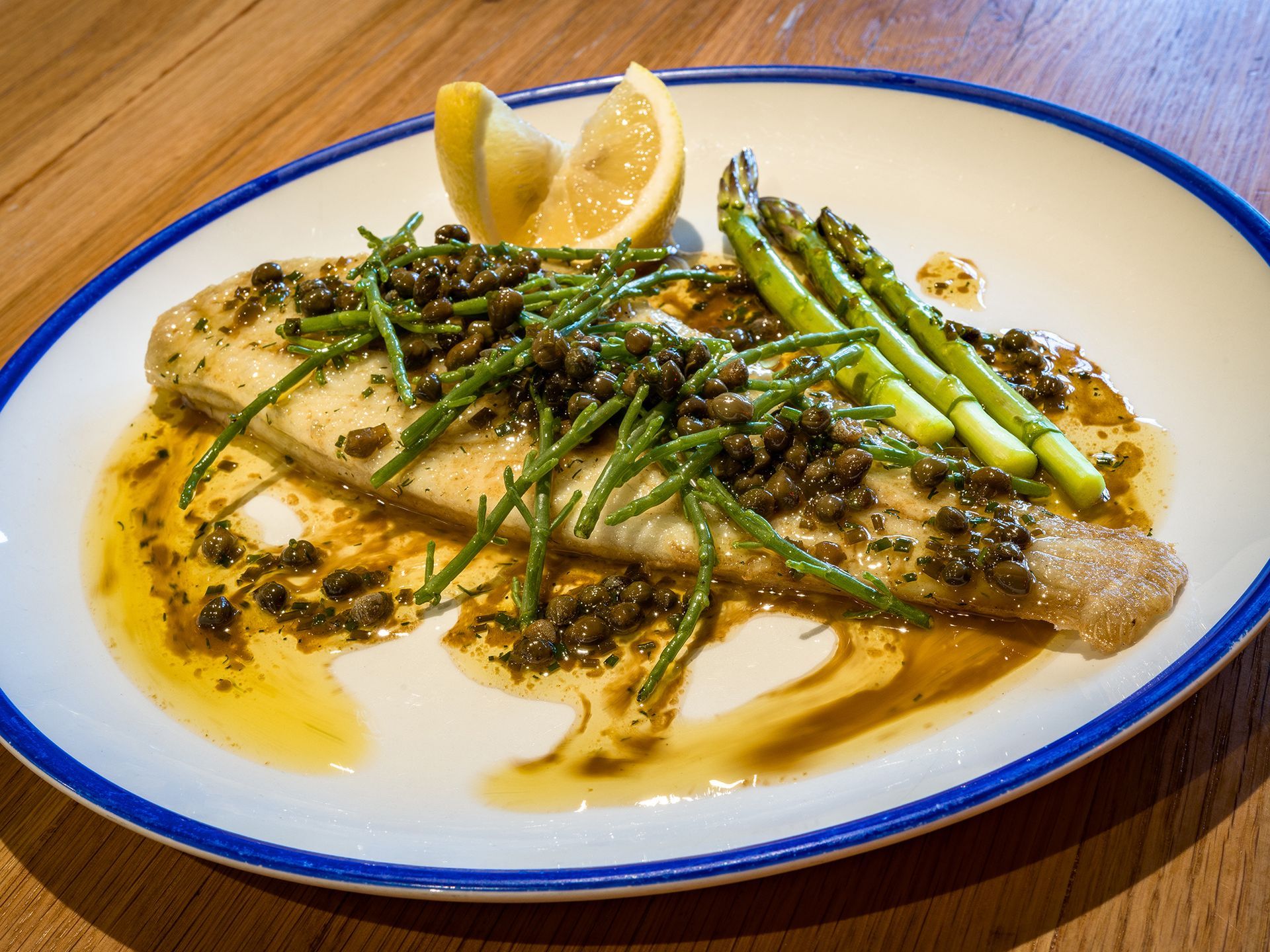 a plate of fish with asparagus and capers on it