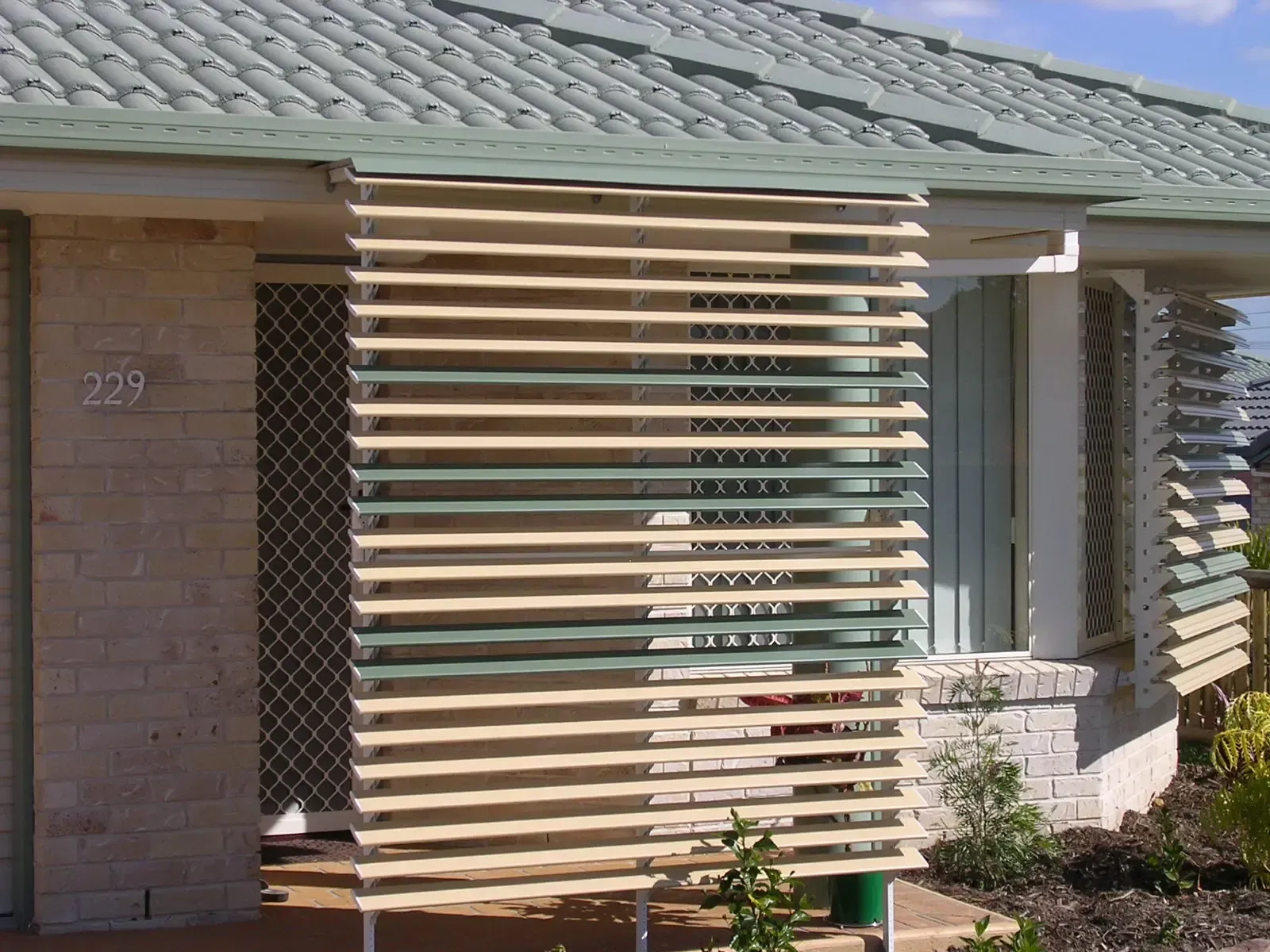 A House Facade With a Patterned Brick Wall and Green Tiled Roof — Advantage Screen And Blinds Rockhampton in Rockhampton, QLD