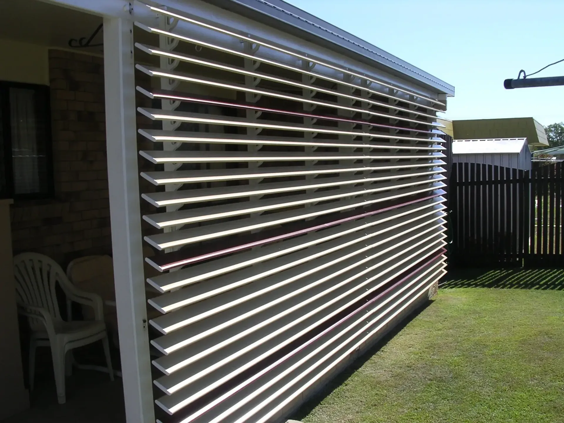 A Shaded Outdoor Patio With White Horizontal Slats — Advantage Screen And Blinds Rockhampton in Rockhampton, QLD