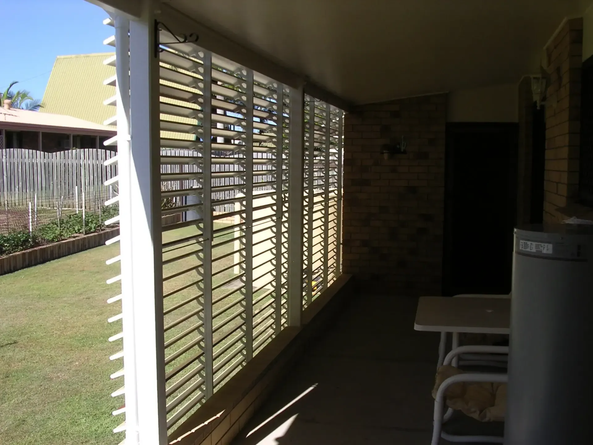 A Sunlit Patio Features White Horizontal Blinds and a Brick Wall — Advantage Screen And Blinds Rockhampton in Rockhampton, QLD