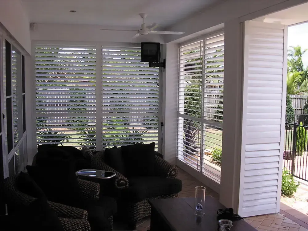 A Sunroom With Cushioned Chairs, a Coffee Table, a Ceiling Fan, and White Louvered Shutters — Advantage Screen And Blinds Rockhampton in Rockhampton, QLD