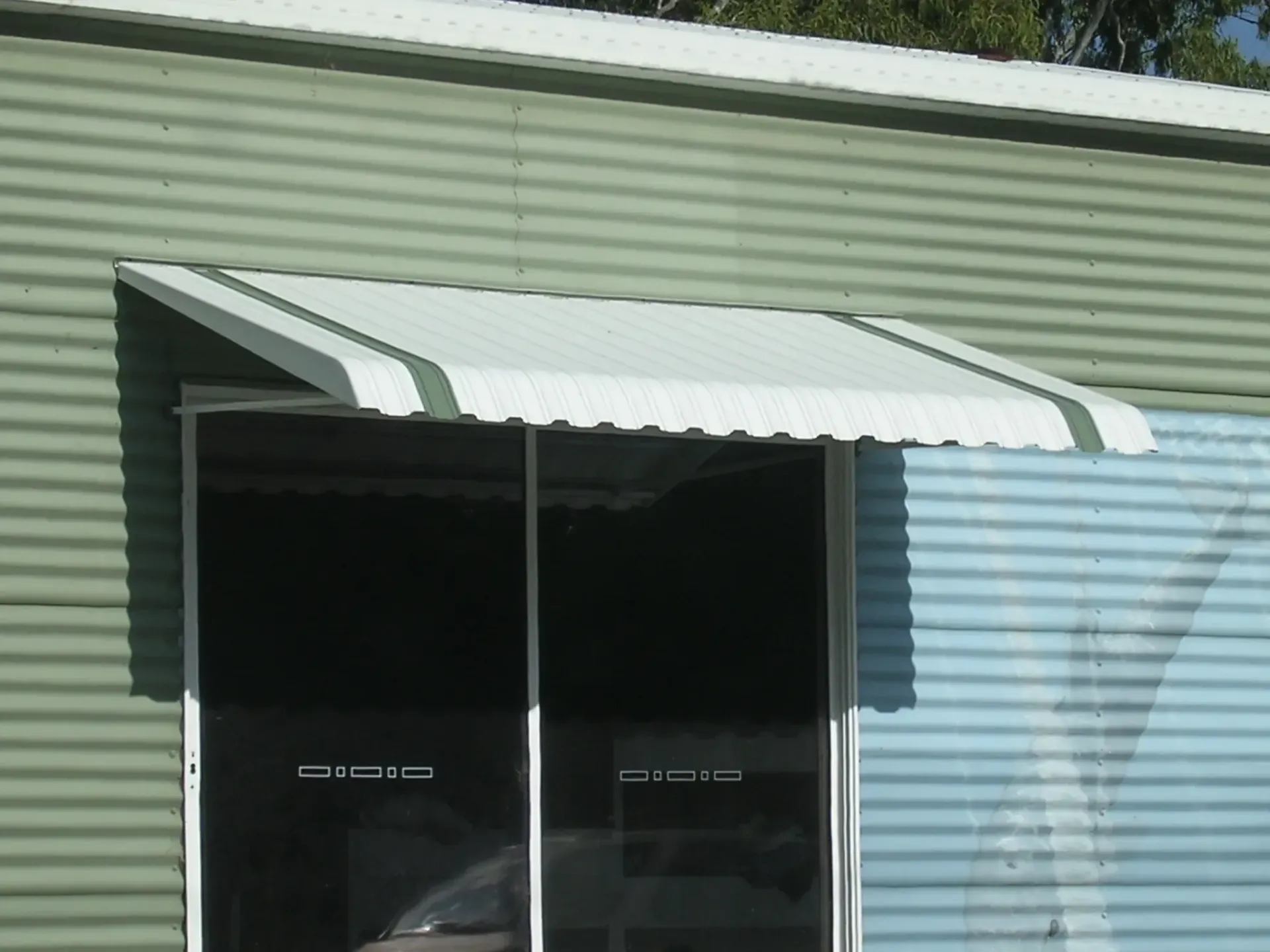 Corrugated Metal Wall With a White Awning Shades Large Windows — Advantage Screen And Blinds Rockhampton in Rockhampton, QLD