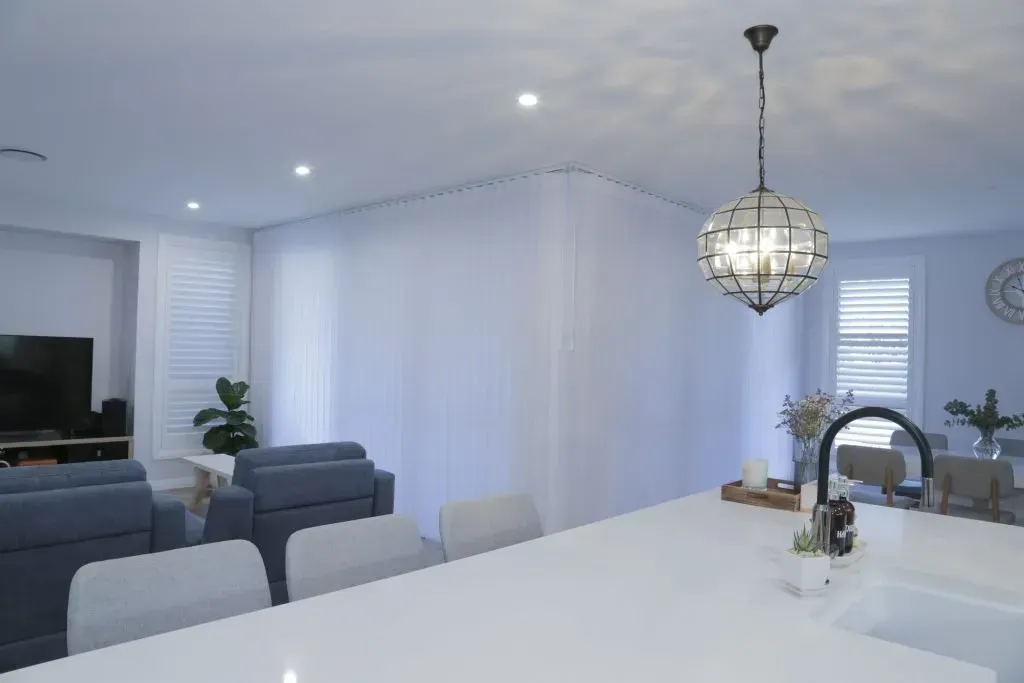 Modern open-plan kitchen and living room with white island, gray chairs, sofa, and pendant light — Advantage Screen And Blinds Rockhampton in Rockhampton, QLD