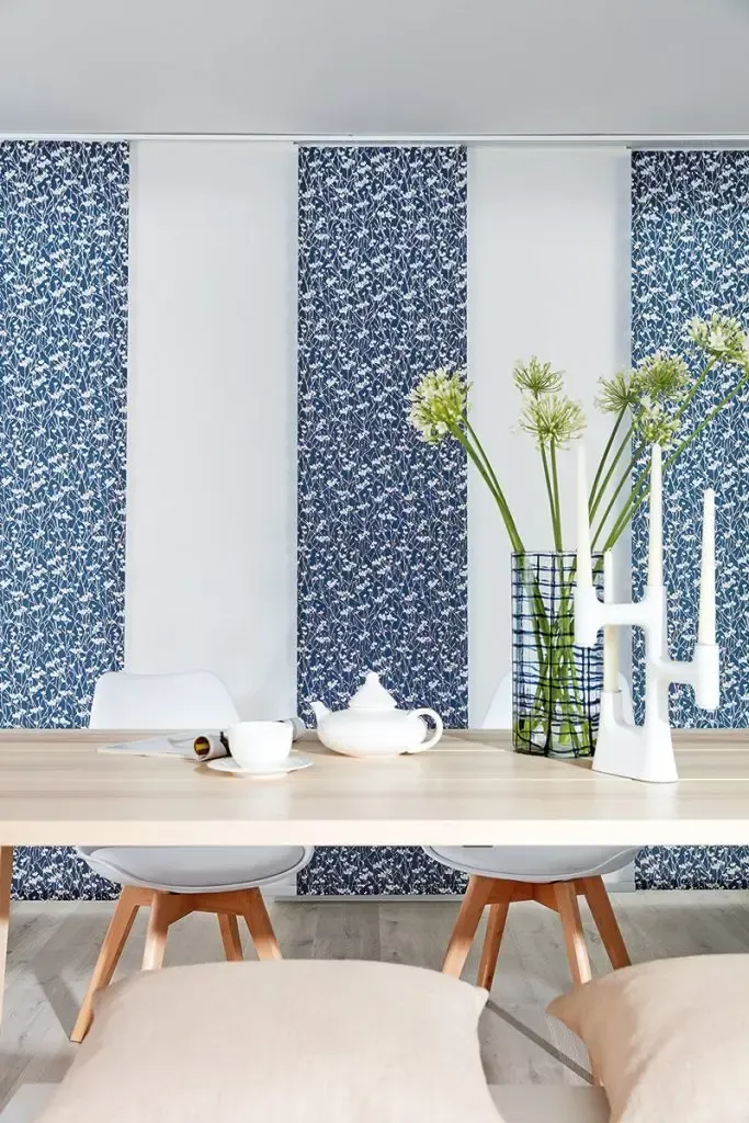 Dining Area With a Light Wood Table Set Against Blue and White Patterned Vertical Blinds — Advantage Screen And Blinds Rockhampton in Rockhampton, QLD