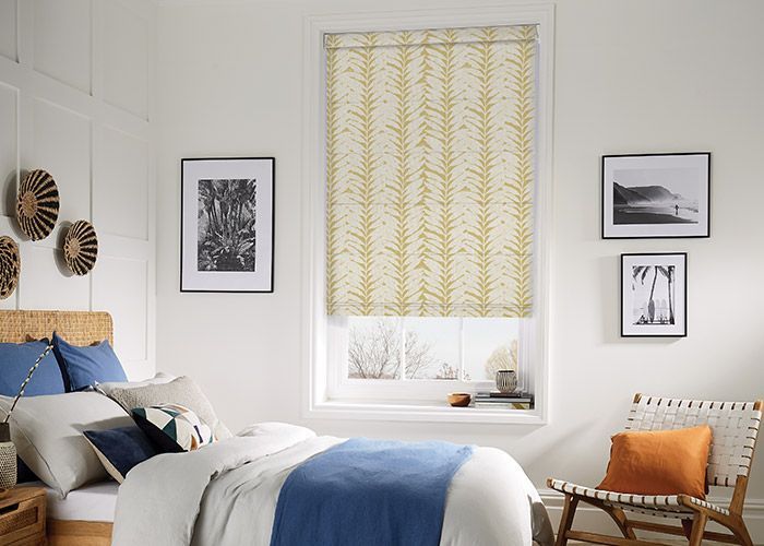 Bright bedroom with blue bedding, white walls, framed art, and a yellow patterned window shade. — Advantage Screen And Blinds Rockhampton in Rockhampton, QLD