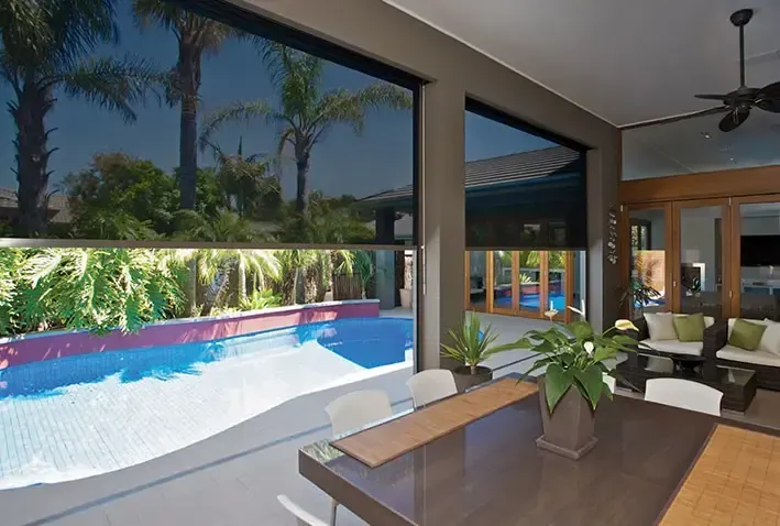 A Covered Patio With Dark Retractable Shades, Overlooking a Swimming Pool and Lush Tropical Landscaping — Advantage Screen And Blinds Rockhampton in Rockhampton, QLD