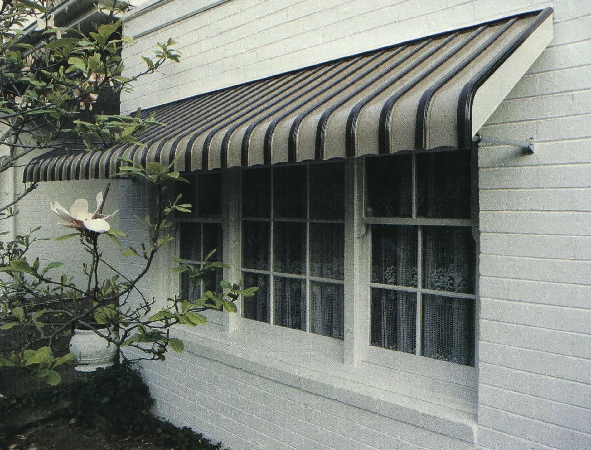 Striped Awning Over a White Brick House Window — Advantage Screen And Blinds Rockhampton in Rockhampton, QLD