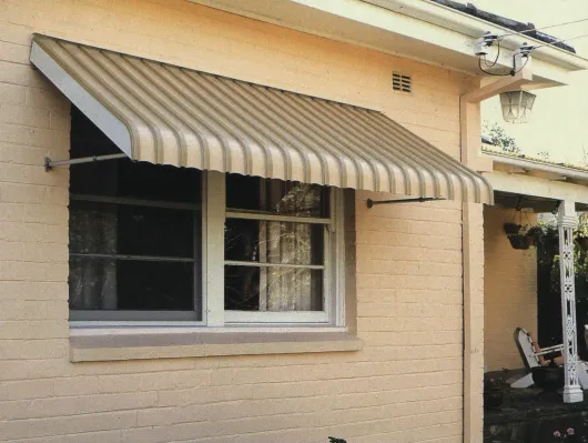 A Tan-striped Metal Awning Installed Over a Window on a Light-colored Brick Exterior Wall — Advantage Screen And Blinds Rockhampton in Rockhampton, QLD