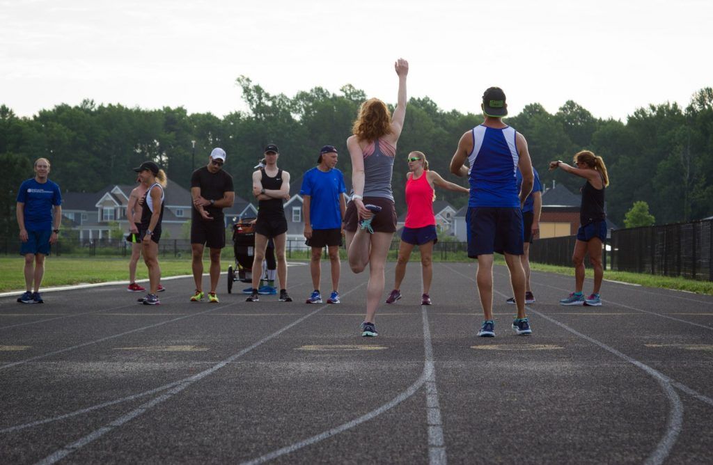 A group of people are standing on a track watching a woman jump in the air.
