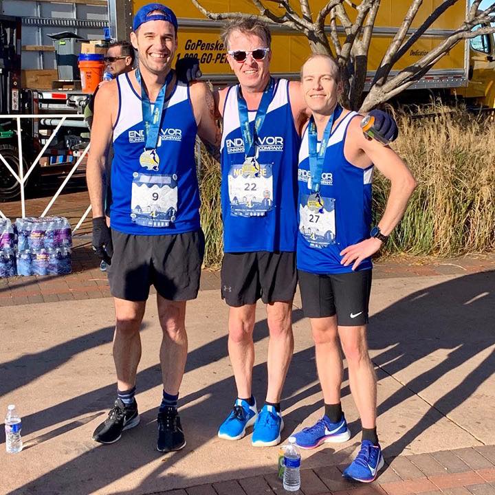 Three men are posing for a picture with medals on their shirts