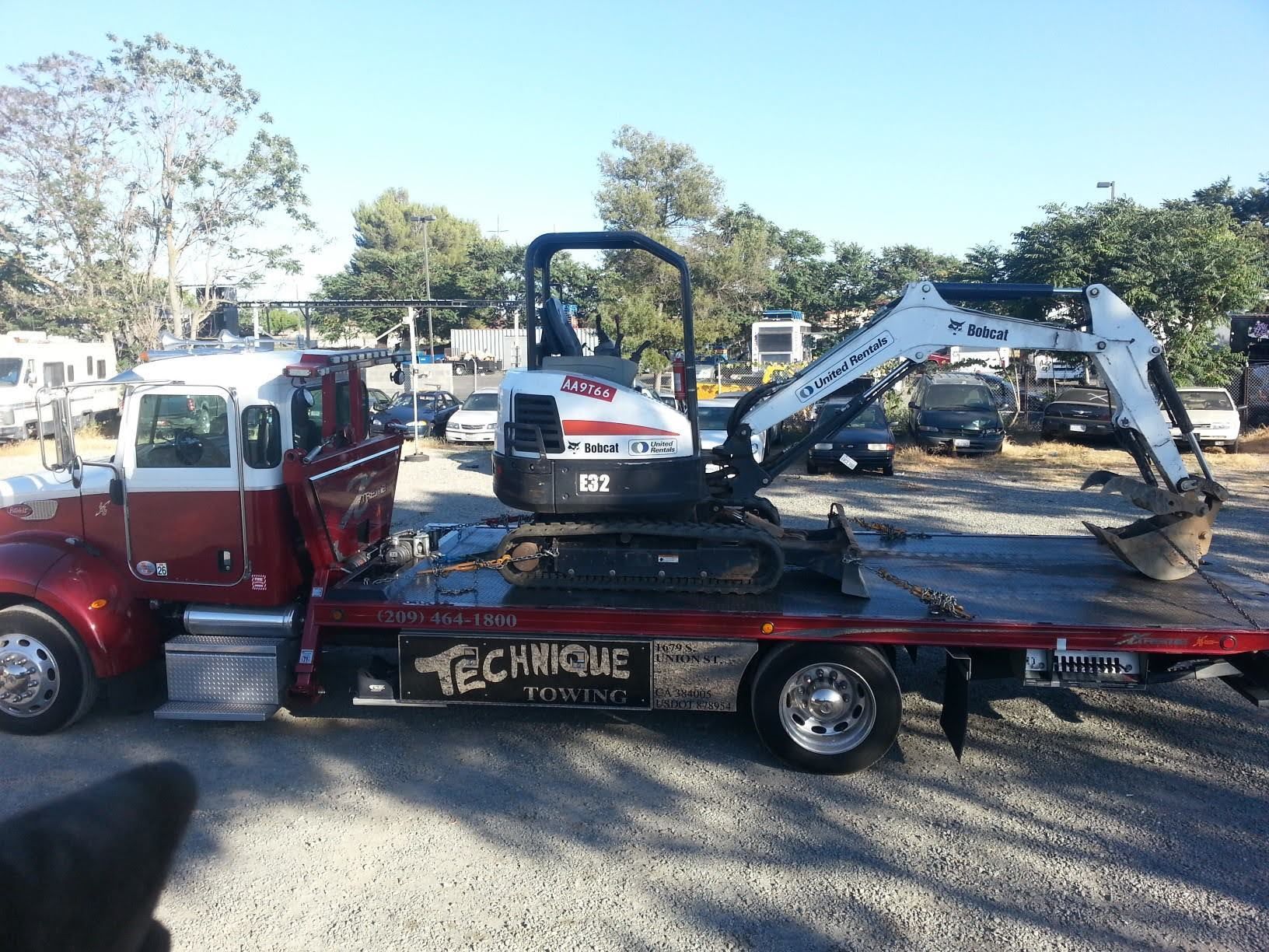 Red and white tow truck carrying a Bobcat excavator. Sunny outdoor setting.