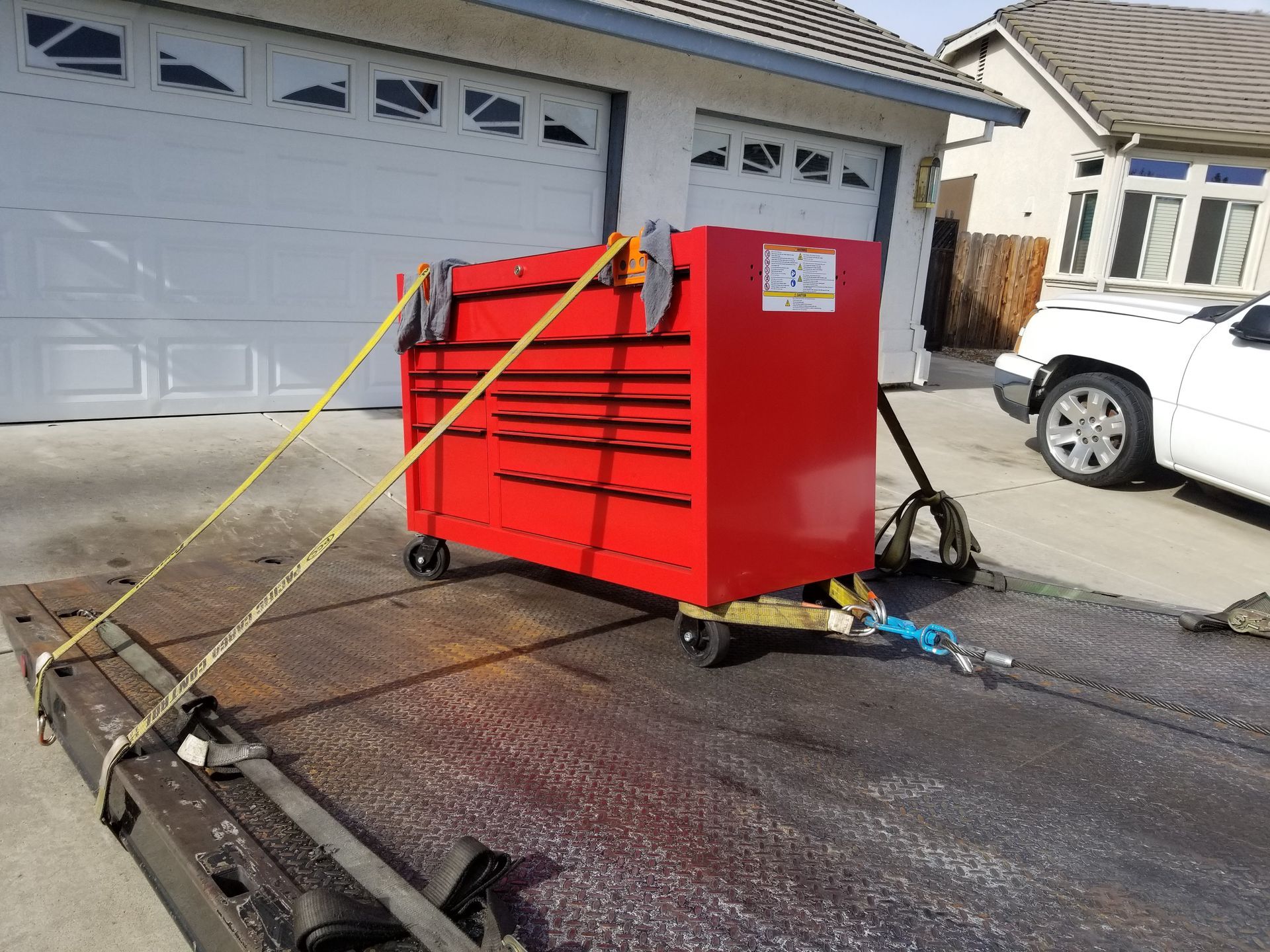 A red toolbox is sitting on a tow truck in front of a garage.