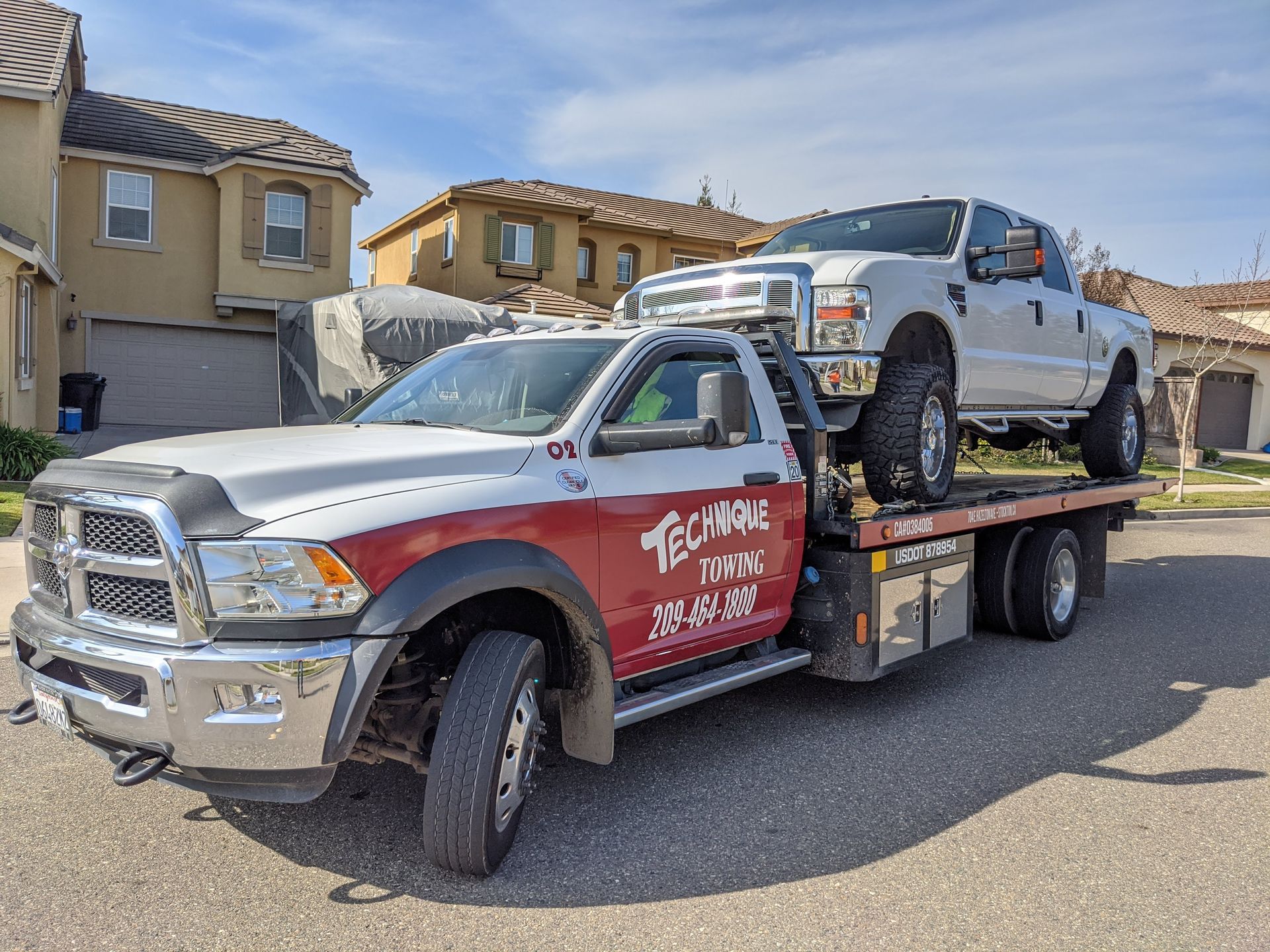 Tow truck carrying a white pickup truck on a residential street.