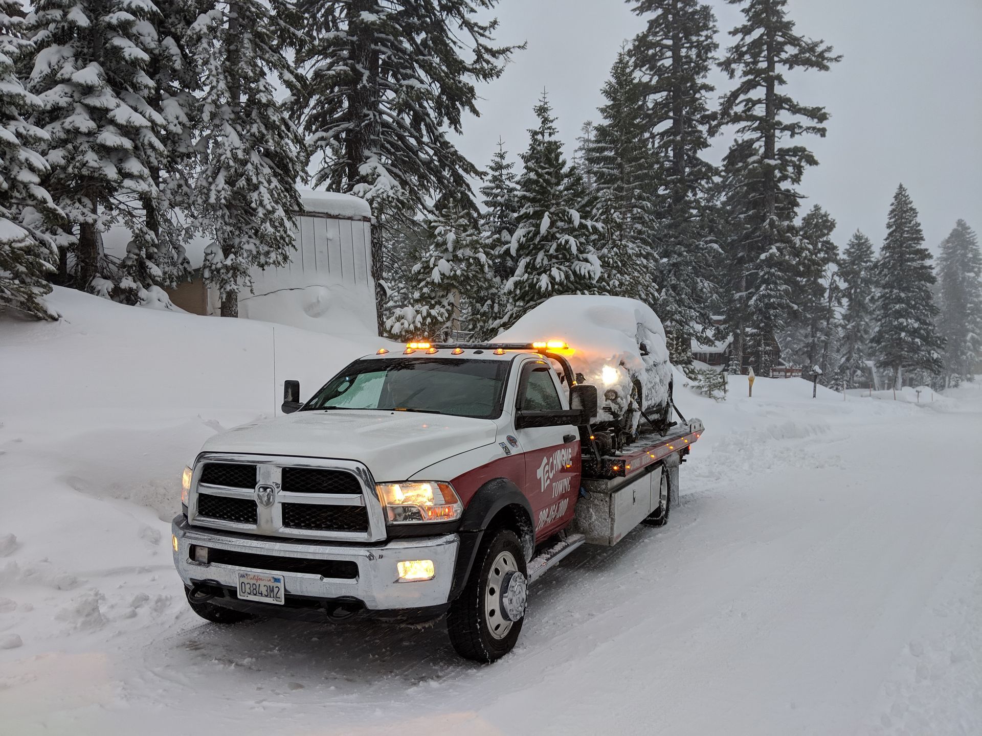 A tow truck with a red car on the back is parked in front of a house.
