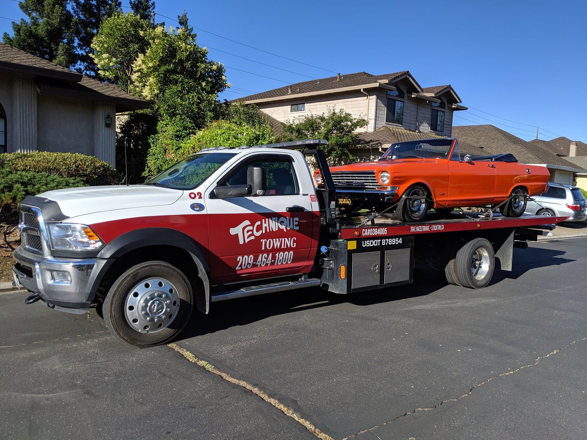 A tow truck with a red car on the back is parked in front of a house.