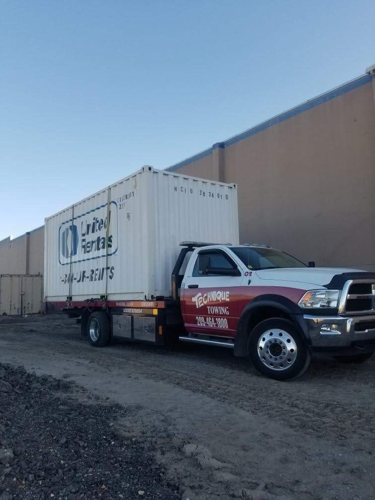 A white truck with a container loaded on the flatbed; parked next to a wall.
