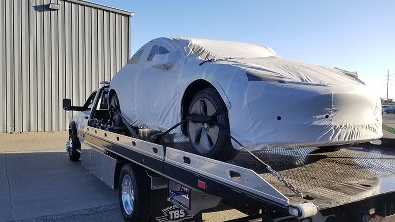 A tesla model 3 is being towed by a tow truck.