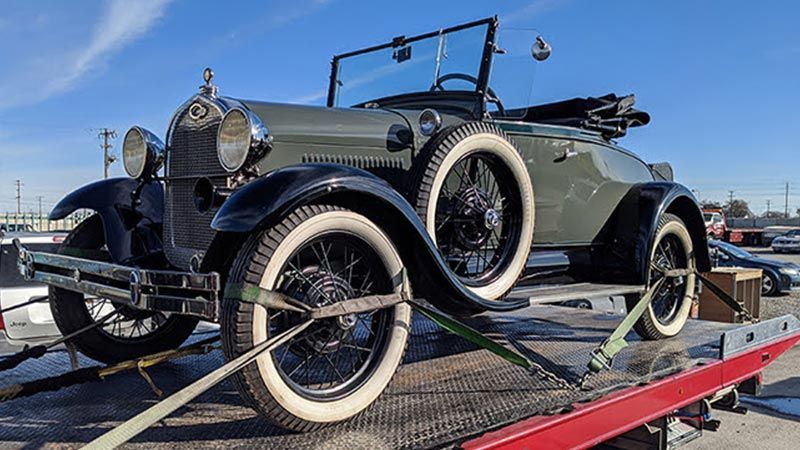 An old car is being towed by a tow truck.