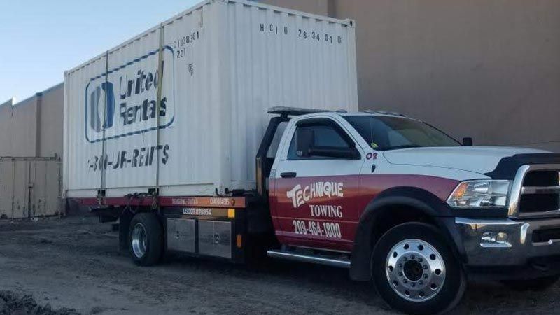 A tow truck with a container on the back is parked in front of a building