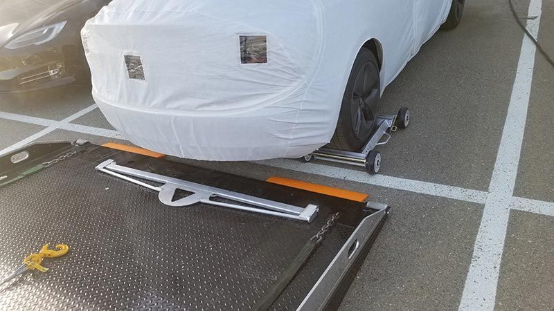 A white car is sitting on a tow truck in a parking lot.