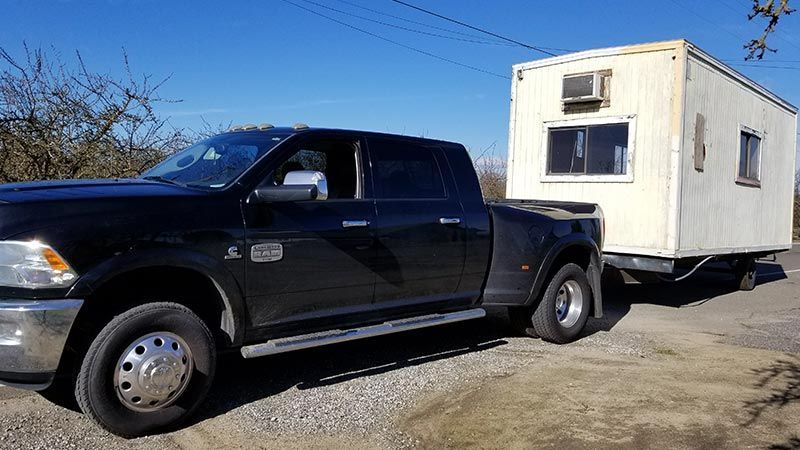 A black truck is towing a small white trailer.
