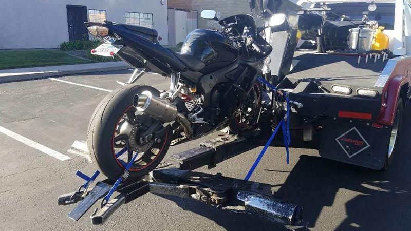 A motorcycle is being towed by a tow truck in a parking lot.