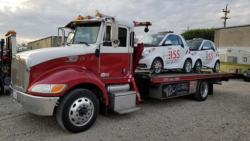 A red and white tow truck with two cars on the back.