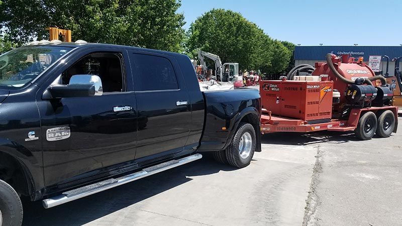 A black truck with a trailer attached to it is parked in a parking lot.