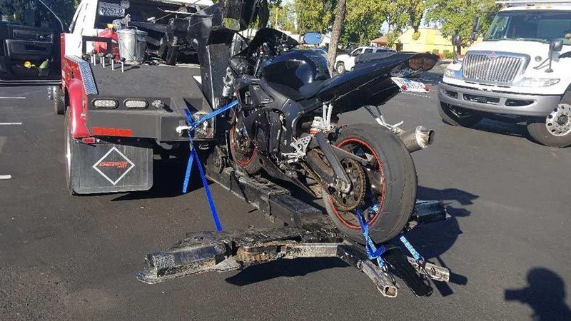 A motorcycle is being towed by a tow truck in a parking lot.
