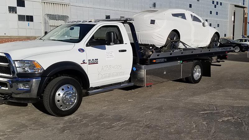 A white tow truck with a car on the back is parked in a parking lot.