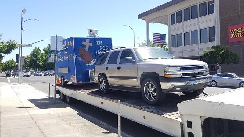 A white tow truck with a car on the back is parked in a parking lot.