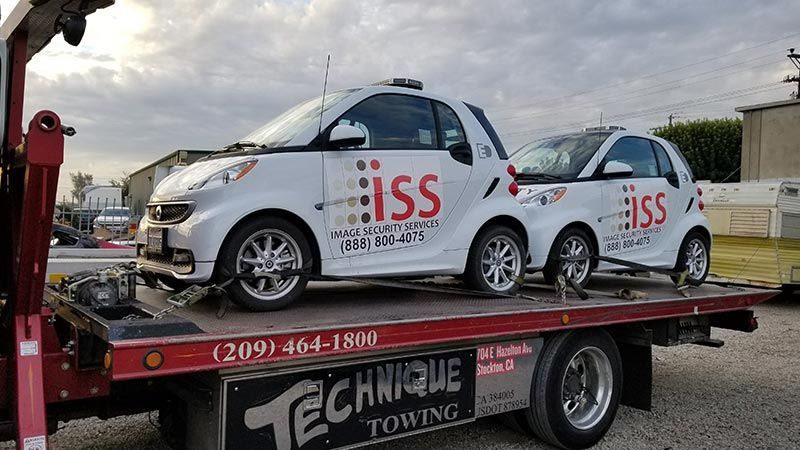 Two smart cars are sitting on top of a tow truck.