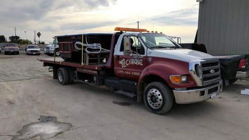 A tow truck with a motorcycle on the back is parked in a parking lot.
