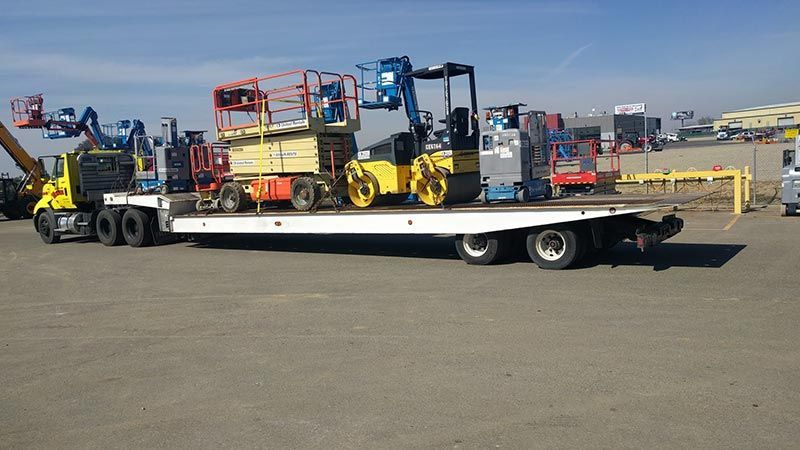A tow truck is carrying a bunch of heavy machinery on a flatbed trailer.