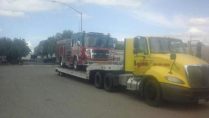 A yellow tow truck is carrying two fire trucks.