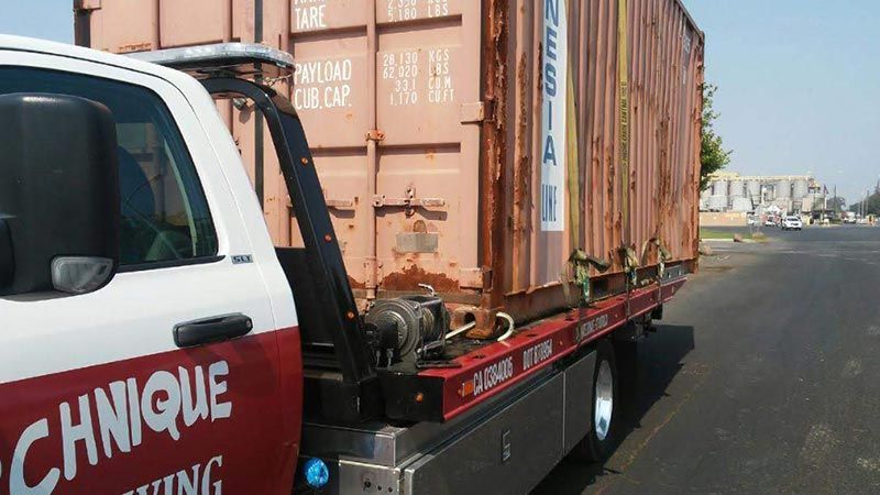 A tow truck is towing a shipping container down the road.