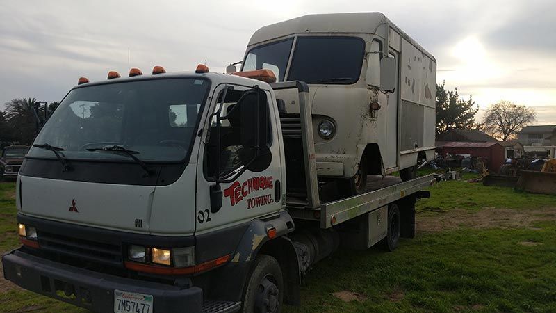 A tow truck is carrying a truck and a trailer on its back.