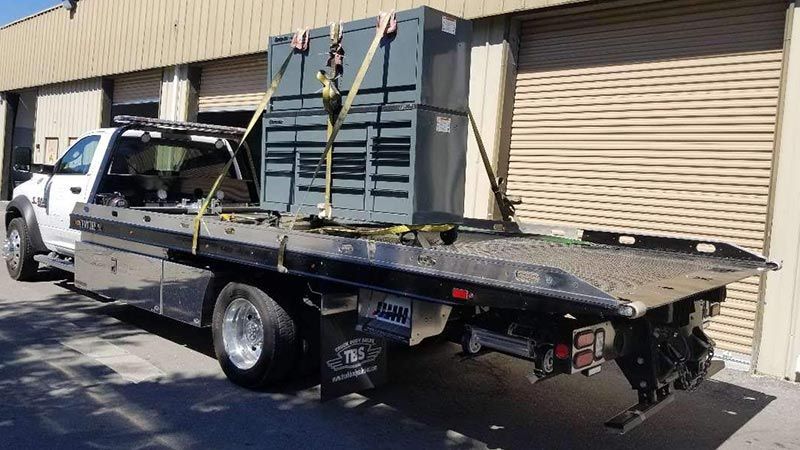 A tow truck with a box on the back is parked in front of a building.
