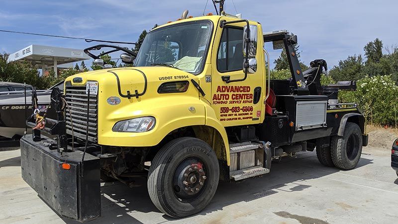 A yellow tow truck is parked in a parking lot next to a gas station.