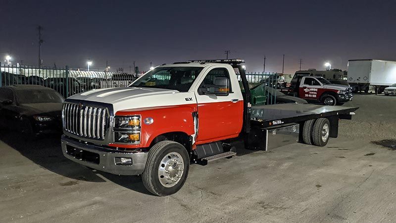 A red and white tow truck is parked in a parking lot at night.