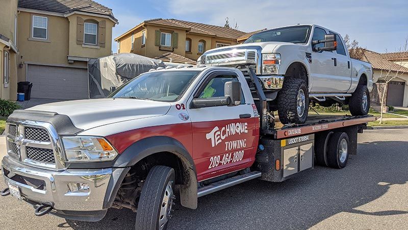 A red tow truck is towing a white rv down a street.