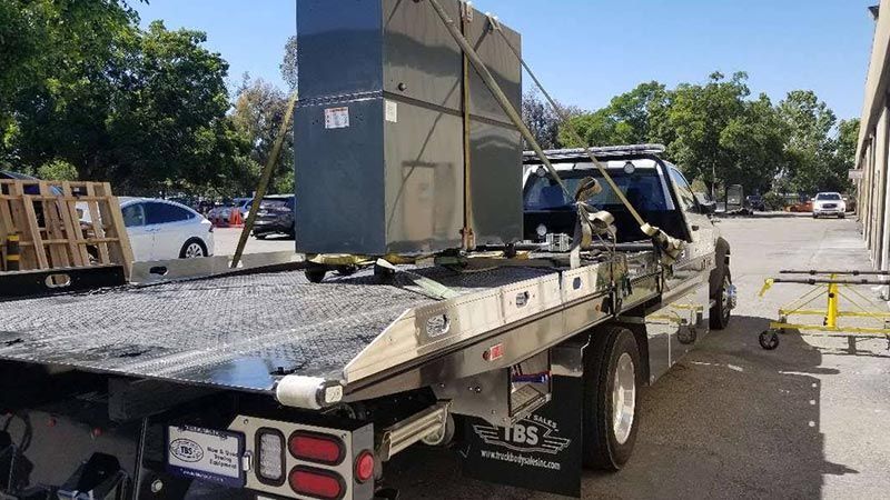 A tow truck is carrying a large box on the back of it.
